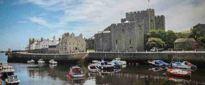 white and red boat on water near gray concrete building during daytime - Castle Rushen is one of the best examples of a medieval castle in Britain. Overlooking the picturesque harbour in the Isle of Man's ancient capital, Castletown, it is now open to the public operated by Manx National Heritage. , tags: cyberhorizon £140,000 man - unsplash